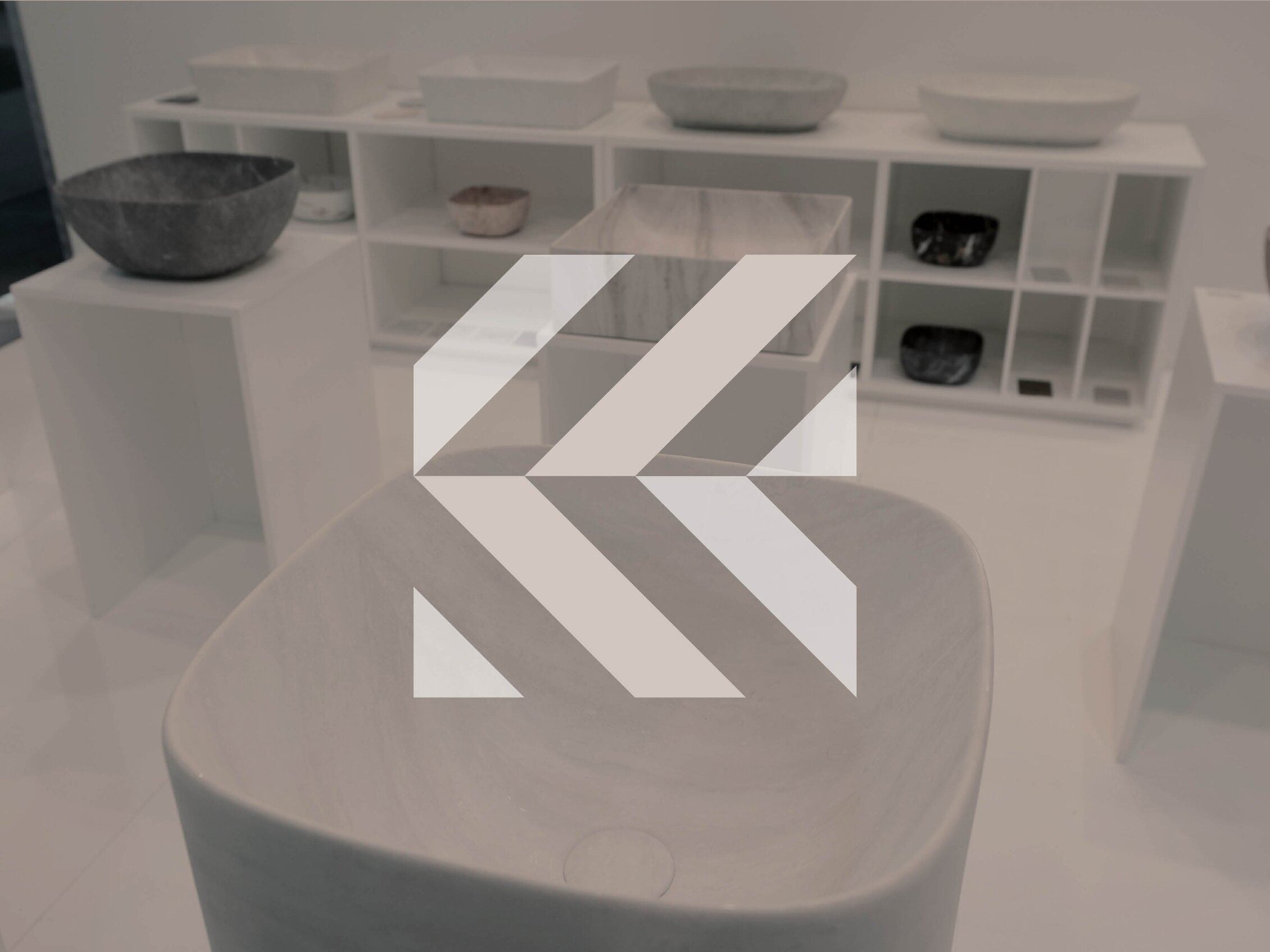 Lavabi e complementi d’arredo in pietra esposti su piedistalli e scaffali bianchi durante una fiera del design e dei materiali.