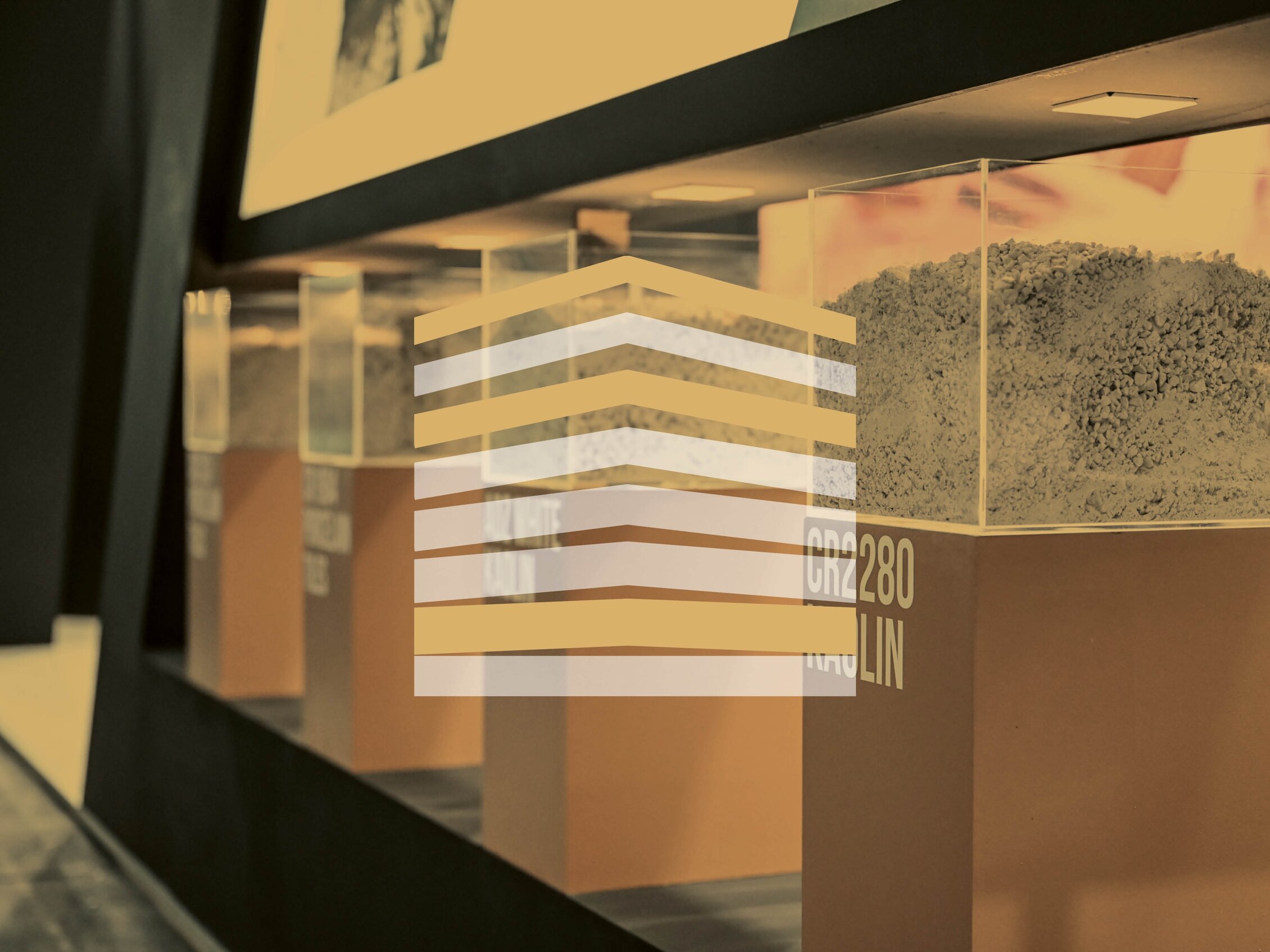 Teche espositive con campioni di materiali granulari e pannelli descrittivi, parte dell’allestimento della fiera dedicata ai materiali e alle tecnologie industriali.