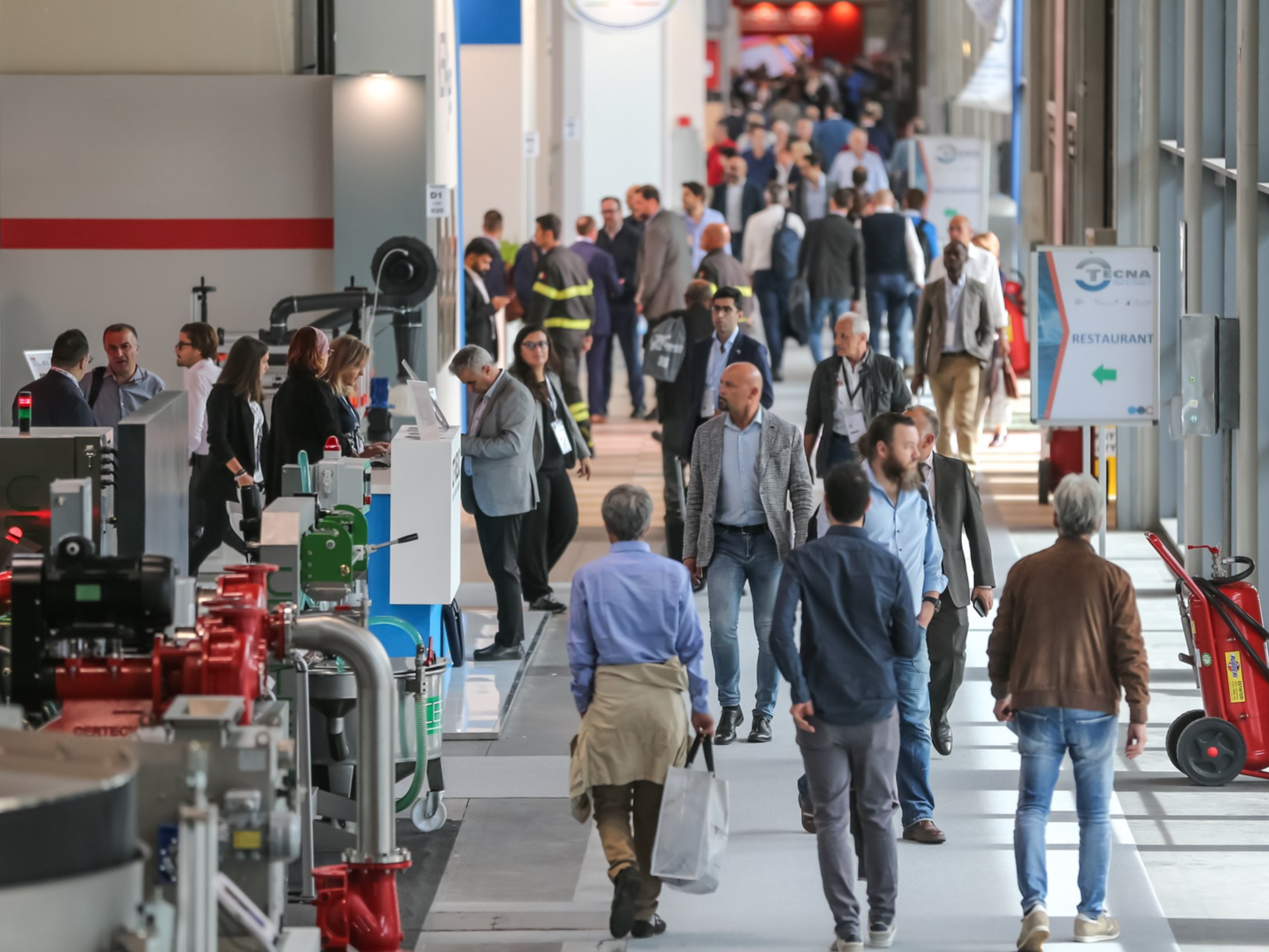 Visitatori che camminano tra gli stand di TECNA, osservando tecnologie e macchinari esposti lungo il corridoio espositivo.
