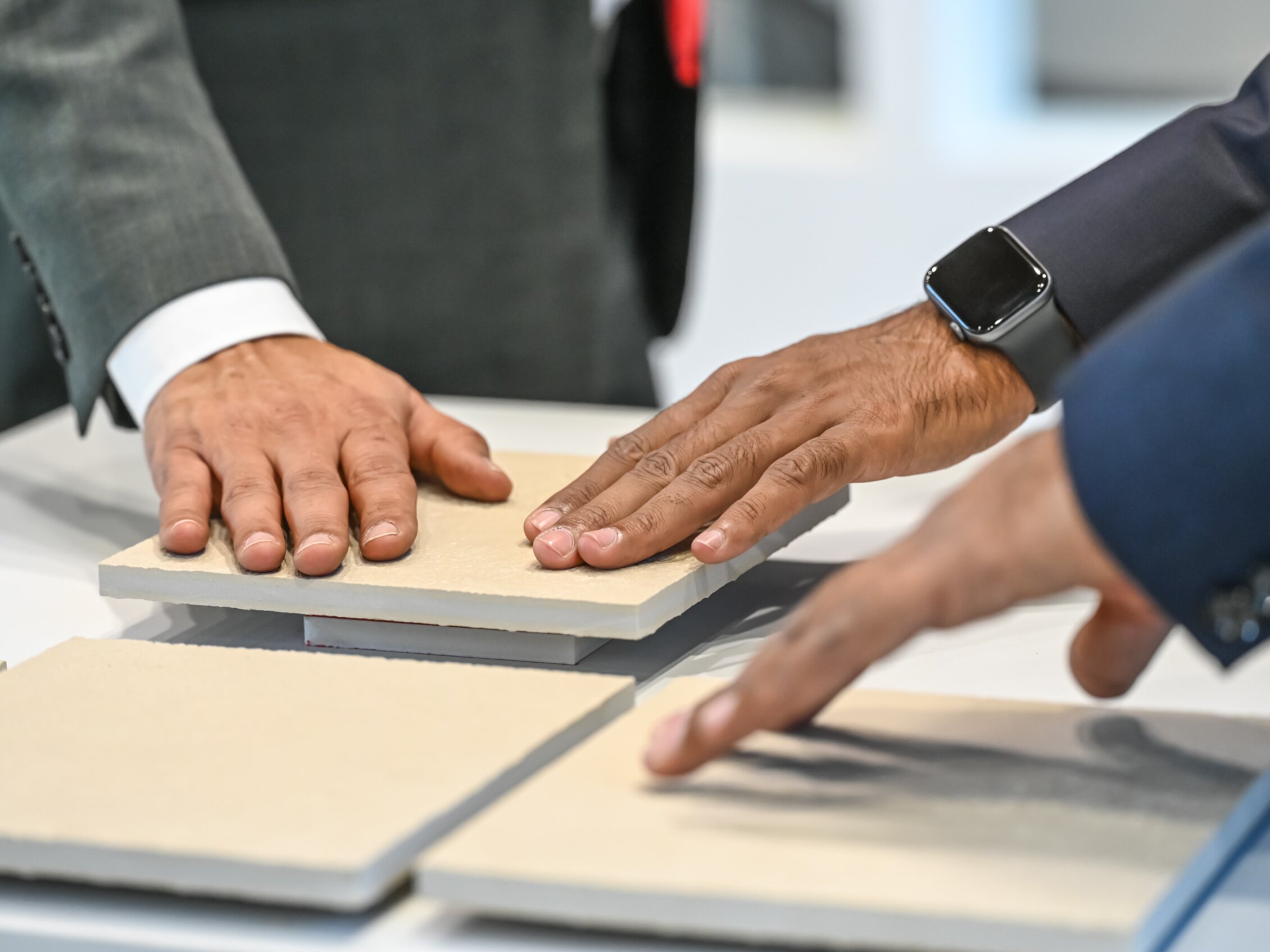 Tre professionisti toccano campioni di piastrelle in ceramica per valutarne texture e qualità durante una fiera.