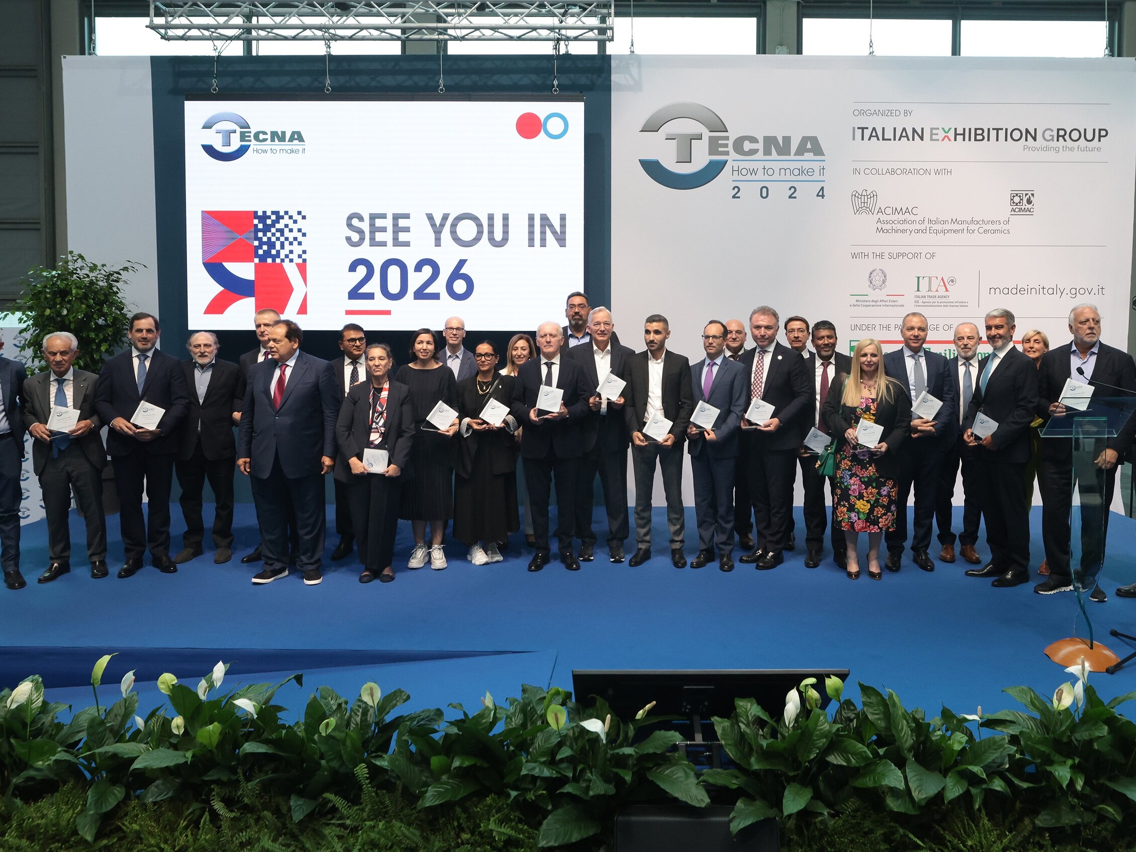Foto di gruppo sul palco con i vincitori del premio a Tecna 2024, ognuno con un riconoscimento in mano, davanti a uno schermo con la scritta “See you in 2026”