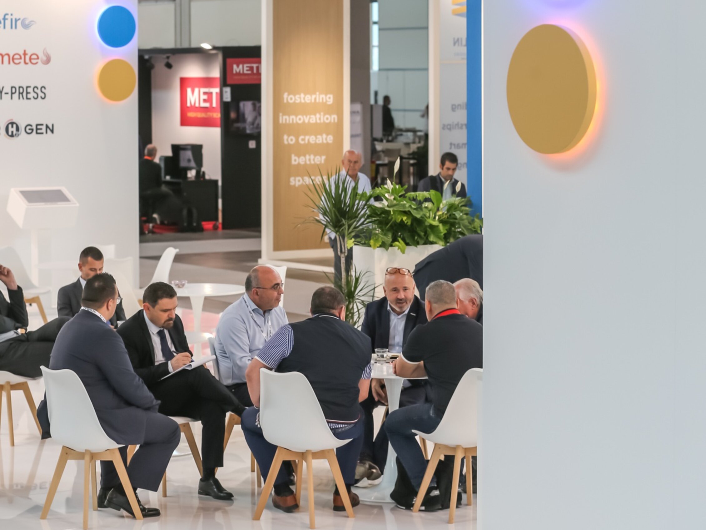 Professionisti seduti in un’area meeting all’interno di una fiera, intenti a discutere opportunità di business tra stand moderni e colorati