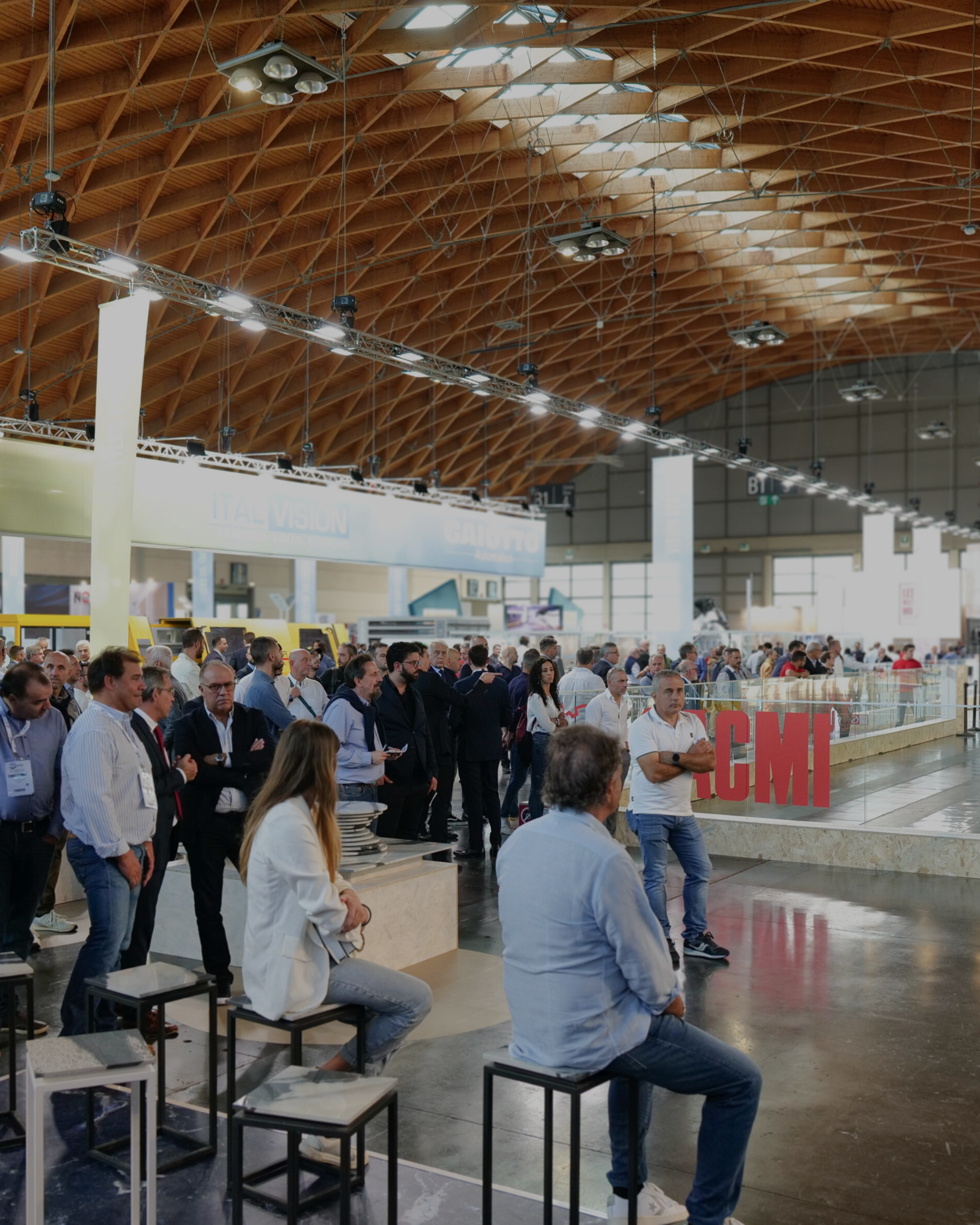 Gruppo di persone in un grande padiglione espositivo con struttura a soffitto in legno.