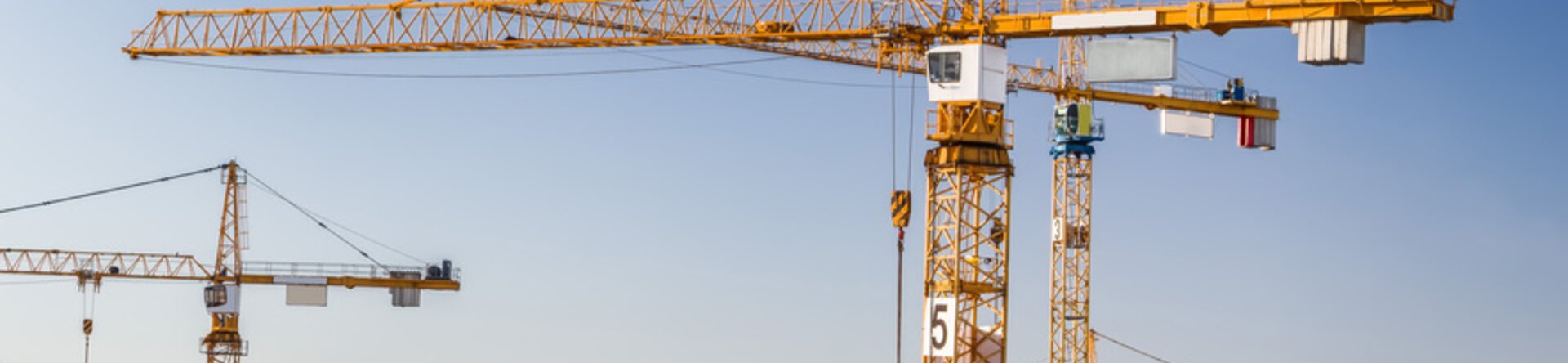 Gru edili gialle in funzione su un esteso cantiere urbano, con edifici in fase di costruzione e cielo sereno sullo sfondo.