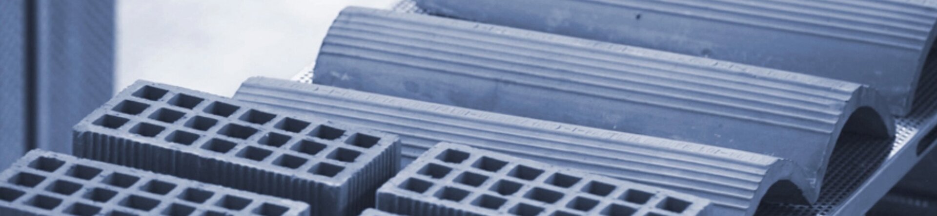 Componenti edilizi in ceramica estrusa, con forme alveolari e curve, posizionati su un nastro di produzione industriale